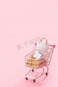 年度销售购物季概念 — 迷你粉色商店推车，里面装满纸袋礼物，浅粉色背景，空白复制空间，特写