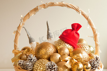 柳条花环摄影照片_巨大的柳条篮子里的金色球，戴着红色圣诞帽。