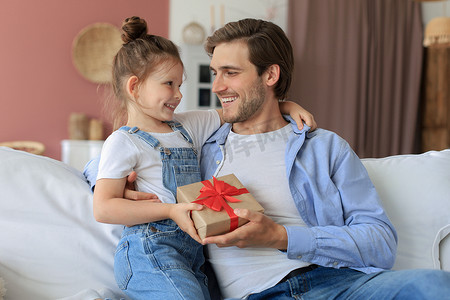 可爱的小女儿给爸爸惊喜，小女孩把礼盒送给坐在沙发上的爸爸。