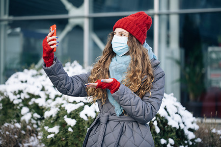 vlog遮罩摄影照片_戴着面罩的女博主正在冬天的时候在街上为她的社交页面制作视频。