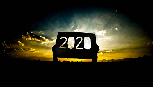 文字2020摄影照片_手握着回收纸板的轮廓，上面写着 2020 年的文字，在日落的天空背景下，阳光透过文字照耀着。