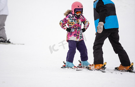 女孩下雪摄影照片_专业的滑雪教练正在教一个孩子在有雪的山坡度假村滑雪一天。