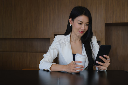 女商人微笑着使用手机，坐在她的办公桌前工作。