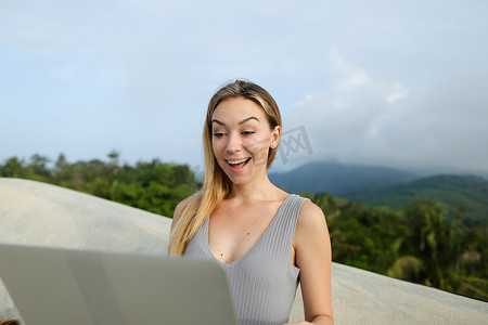年轻漂亮的女性在山区背景下使用笔记本电脑，穿着灰色衬衫。
