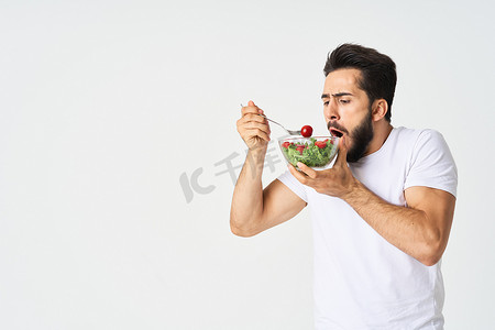 穿着t恤的人摄影照片_一个穿着白色T恤的男人，盘子里放着沙拉和零食健康食品