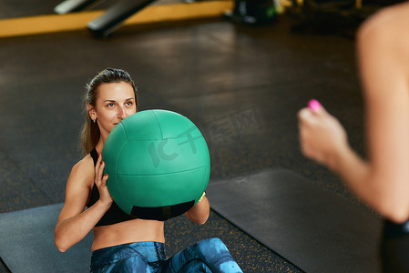 在私人教练的协助下，身穿运动服的年轻运动女性在健身房用健身球进行腹肌锻炼