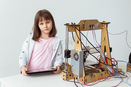 3d打印设计摄影照片_带着 3D 打印快门色调的可爱女孩正在看着她的 3D 打印机打印她的 3D 模型。