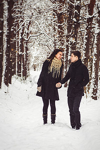 冬天总结摄影照片_一个穿着暖和的衣服和围巾的男孩和女孩在雪天散步