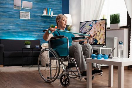 轮椅下坡摄影照片_轮椅抱阻弹力带拉伸身体肌肉的无效老年妇女