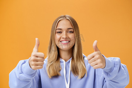 快乐乐观女性的画像竖起大拇指，微笑着支持，脸上带着欢快的表情，赞同并喜欢伟大的产品，在橙色的墙上给出积极的意见和推荐