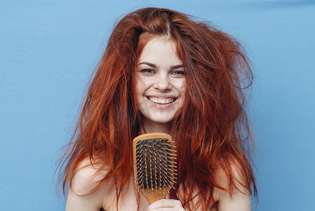 裸肩的女人，凌乱的红发，梳子蓝色背景