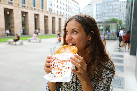 快乐的年轻女商人在她短暂的午休时间吃一个小披萨。