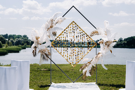 举行婚礼摄影照片_在大自然中装饰的婚礼拱门。在湖背景上用复古风格的羽毛装饰的拱门举行婚礼