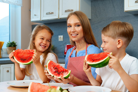 甜蜜的家庭、母亲和她的孩子在厨房里吃西瓜玩得开心