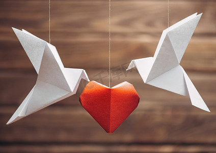两个折纸鸽围绕着红纸心，情人节贺卡。