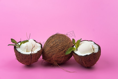 白色冰淇淋球摄影照片_粉红色背景中用薄荷叶装饰的新鲜椰子半香草冰淇淋球