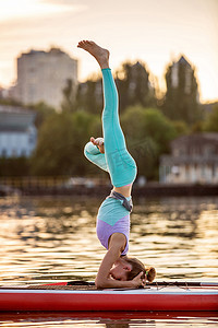 灵活性摄影照片_运动型女性在桨板上做瑜伽，在垫板上做瑜伽，锻炼灵活性和伸展肌肉