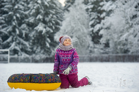一个冬天穿着紫色衣服和充气圈的小女孩在白雪覆盖的森林里走在街上