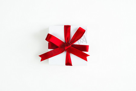 美丽的节日或圣诞节背景图像，是一个小红丝带包裹着白色盒子的礼物，以白色背景为中心，礼物周围有复制空间。