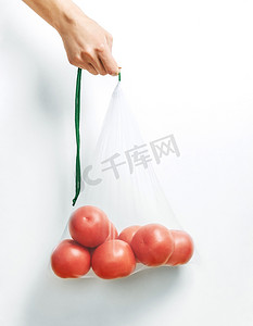 手拿着一个可重复使用的生态袋和西红柿。