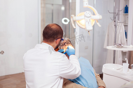 老人用牙线剔牙摄影照片_在牙科诊所修牙的高级病人