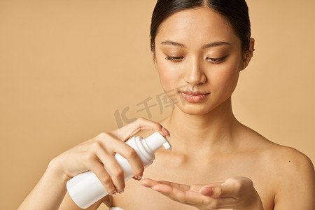 温和的摄影照片_工作室肖像中自然年轻女性拿着一瓶温和的泡沫洁面乳，隔离在米色背景中