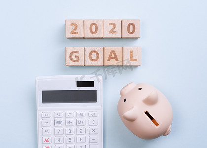 摘要 2020 年财务目标设计概念 — 蓝桌背景上的几何木块立方体，带有存钱罐、顶视图、平躺、复制空间。