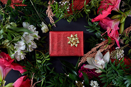 红色暗色摄影照片_带礼物的红色盒子被鲜花包围