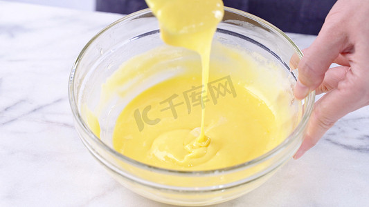 用绿色橡胶抹刀混合器工具将蛋黄混合到蛋糕糊中，搅拌直至光滑并在玻璃碗中充分混合，特写，生活方式