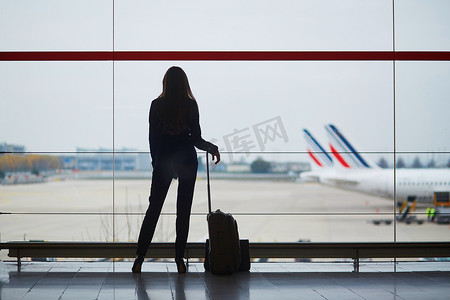 透过窗户的光摄影照片_国际机场提着手提行李的女士透过窗户看飞机