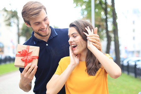 站在城市街道上，穿着夏装的一对兴奋的夫妇微笑着拿着礼物盒在一起。