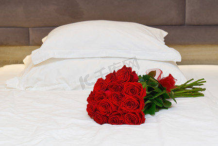 在酒店房间度蜜月的床上放着一束红玫瑰。