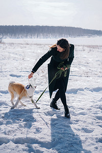 带绿色皮带的秋田犬和穿深绿色外套的女人玩绳索玩具