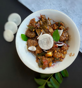 鸡块摄影照片_美味的印度风格辣辣椒羊肉精美地放在白色碗中，镀有黑白彩色纸，配上洋葱和咖喱叶，对骨头有益