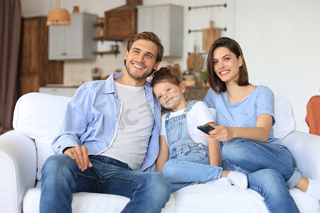 幸福的家庭，孩子坐在沙发上看电视，年轻的父母抱着女儿一起在沙发上放松。
