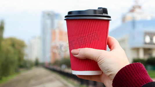 在寒冷的季节，一个小女孩手里拿着一个红色的一次性纸杯，手里拿着咖啡或其他热饮。