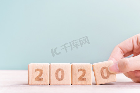 2023兔年来了摄影照片_摘要 2020 年和 2019 年新年倒计时设计理念 — 女性在木桌和绿色背景上拿着木块立方体，特写，复制空间。