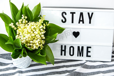 白桶摄影照片_灯箱上写着“待在家里”，并在白桶里放上铃兰花束，春天