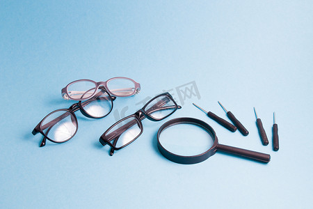 放大镜儿童摄影照片_放大镜、几副眼镜和小螺丝刀在蓝色背景上，正在修理儿童眼镜和成人眼镜