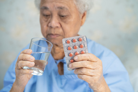 中老年声乐摄影照片_亚洲老年或老年老妇人妇女患者在医院治疗感染患者的泡罩包装中持有抗生素胶囊药丸，药房药房概念。