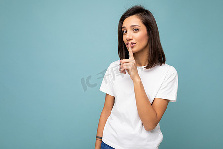 年轻迷人的黑发女性的画像，带着真诚的情感，穿着休闲的白色 T 恤，在蓝色背景中与复制空间隔离并询问保持沉默