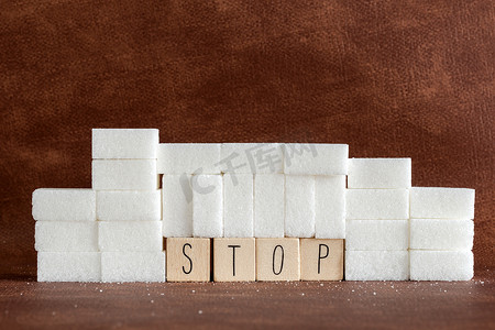 堆或墙的糖块和大写字母的停止词，作为对成瘾卡路里过量和甜味不健康食物滥用导致健康问题和超重背景的建议