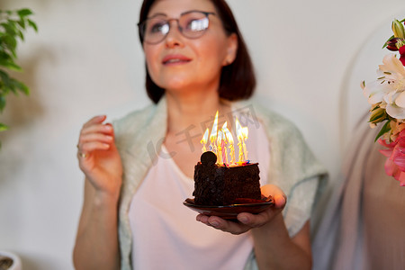 有小生日蛋糕的成熟妇女与燃烧的蜡烛