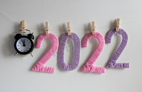 时钟一月摄影照片_时钟和数字 2022 由白色背景上的粉红色和淡紫色线制成，挂在衣夹上。