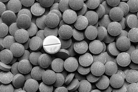 一堆深色药丸围绕着一个白色药丸，低调的单色。