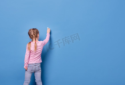 黑板蓝色背景摄影照片_小女孩在蓝色背景上用粉笔写字