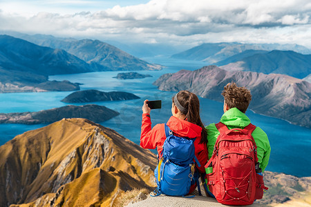 学校踩踏摄影照片_徒步旅行者在徒步旅行度假时欣赏山顶风景 — 情侣用手机拍照。