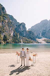 白云站摄影照片_新娘和新郎在意大利 Lago di Braies 的背景下，以秋天的花柱拱门为仪式站好。