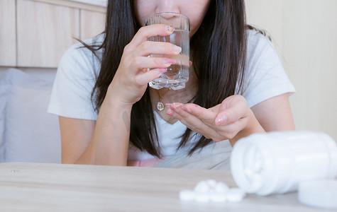真人吐血摄影照片_感染感冒的流感药妇女将药物放在桌子上和一杯水上。