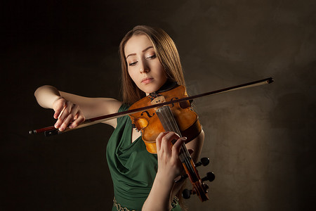 小提琴中提琴摄影照片_美丽的年轻女子在黑色背景上拉小提琴